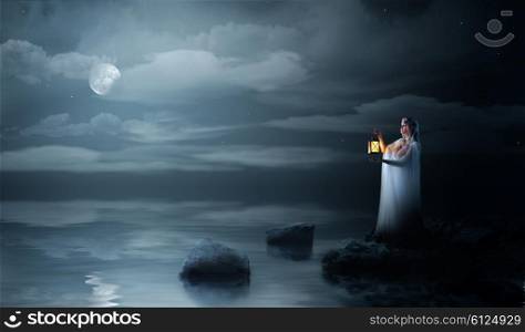 Young elven girl with lantern at night sea shore