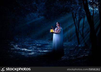 Young elven girl with lantern in night forest