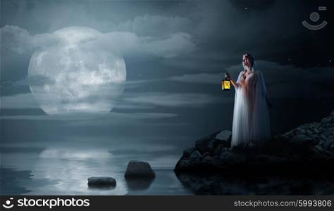 Young elven girl with lantern on night sea coast