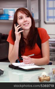 young employee is calling and writing notes on her diary, on the desk there are some nozzles