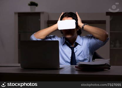 Young employee with virtual glasses at night in the office 