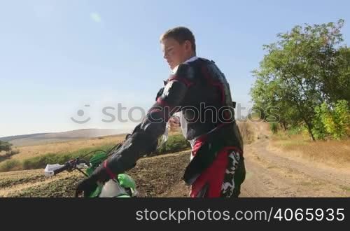 Young enduro racer dressing motorcycle protective gear beside his dirt bike