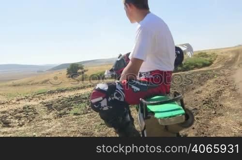Young enduro racer sitting on dirt bike looking away, jib crane shot