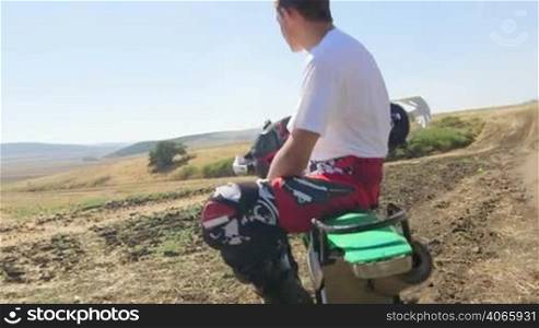 Young enduro racer sitting on dirt bike looking away, jib crane shot