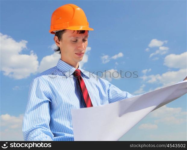 young engineer in blue shirt and yellow helmet against blue sky