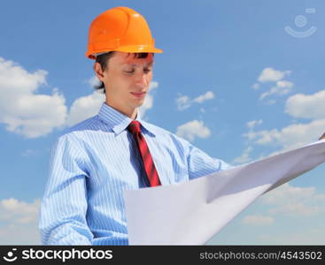 young engineer in blue shirt and yellow helmet against blue sky