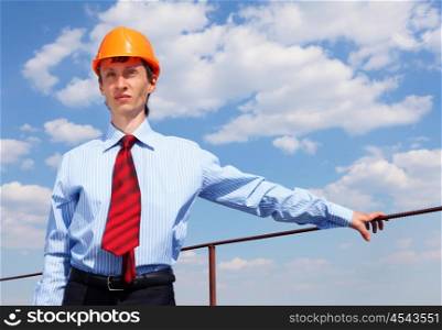 young engineer in blue shirt and yellow helmet against blue sky
