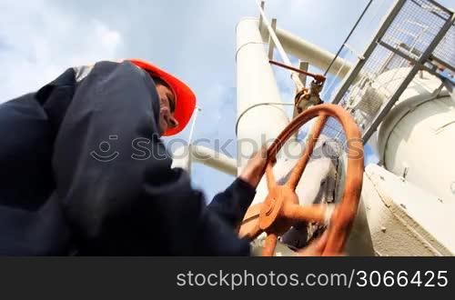 young engineer in orange helmet close valve on gas cleaning installation, close-up from below