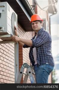 Young engineer installing air conditioner on building outer wall