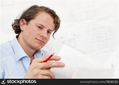 Young engineer reviewing a stack of technical drawings, with more complex designs in the background