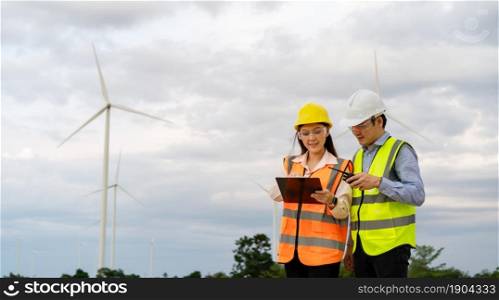 young engineer team working with report in clipboard against wind turbine farm