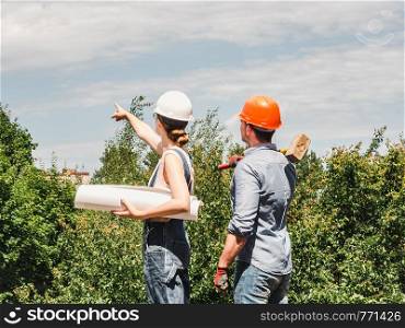 Young engineer woman and her subordinate worker holding a paper project in the park against the backdrop of green trees. Close-up. Concept of labor and employment. Young engineer woman and her subordinate worker