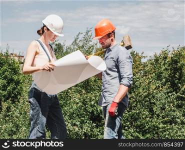 Young engineer woman and her subordinate worker holding a paper project in the park against the backdrop of green trees. Close-up. Concept of labor and employment. Young engineer woman and her subordinate worker