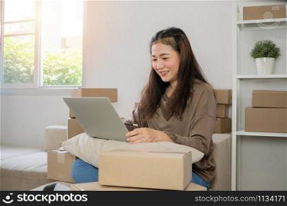Young entrepreneur, sitting on the sofa and working at home. Checking orders from customers by laptop and writing customer address deliver shipment online sales. Concept of small business owner.