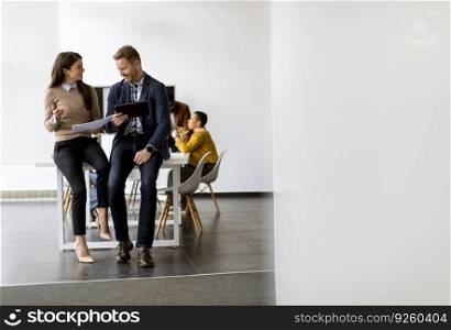 Young entrepreneurs sitting together on a desk and using digital tablet in the modern office