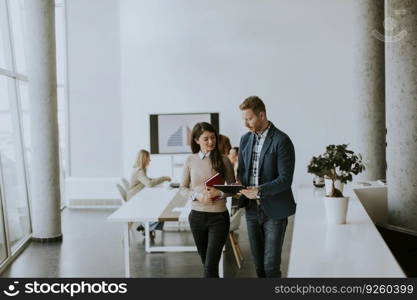 Young entrepreneurs walking together and using digital tablet in the modern office