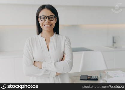 Young european executive or ceo in glasses and white blouse is working remote from home. Confident girl, entrepreneur is standing with her arms crossed and smiling. Career and leadership concept.. Young european executive or ceo standing with her arms crossed and smiling. Career and leadership.