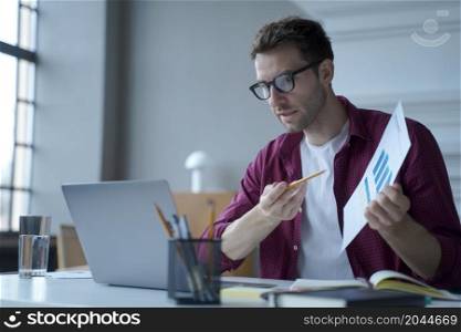 Young european man office worker in glasses showing statistics report during online meeting with business partner, german guy financial advisor consulting client remotely from home, using laptop. Young european man office worker in glasses showing statistics report during online meeting