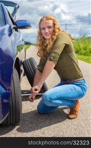 Young european woman changing car tire on rural road