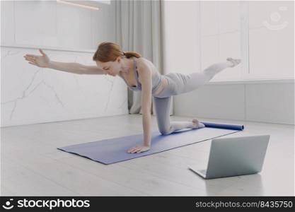 Young european woman enjoying yoga by video lessons and stretching hand. Posture exercise. Internet learning with computer. Gymnastics at home classes. Morning exercise and sport routine concept.. Young woman enjoying yoga by video lessons. Morning exercise and sport routine concept.