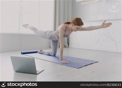 Young european woman enjoying yoga by video lessons and stretching hand. Posture exercise. Internet learning with computer. Gymnastics at home classes. Morning exercise and sport routine concept.. Young woman enjoying yoga by video lessons. Morning exercise and sport routine concept.
