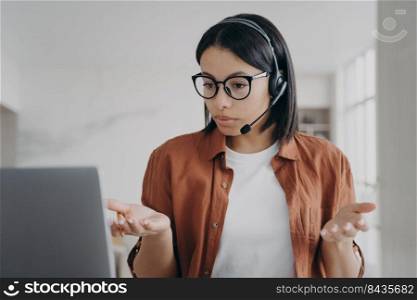 Young european woman has online conference. Businesswoman in headset and glasses is talking. Manager or business assistant is sitting at the desk and having interview. Confident girl at workplace.. Young european woman has online conference or interview. Businesswoman in headset is talking.