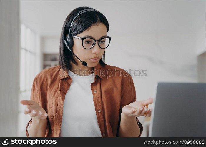 Young european woman has online conference. Businesswoman in headset and glasses is talking. Manager or business assistant is sitting at the desk and having interview. Confident girl at workplace.. Young european woman has online conference or interview. Businesswoman in headset is talking.