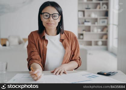 Young european woman in glasses is working remote. Confident manager is doing research at home. Happy business assistant is sitting at the desk and doing paperwork. Strategy planning, data analysis.. Manager doing research at home. Happy business assistant is planning strategy, doing data analysis.