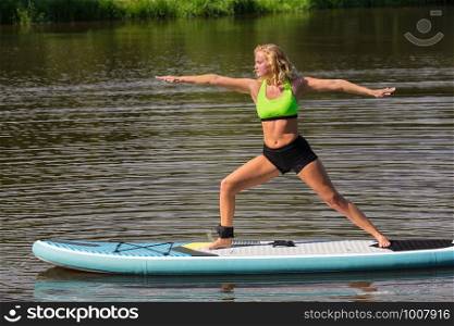 Young european woman on SUP in yoga posture on pond