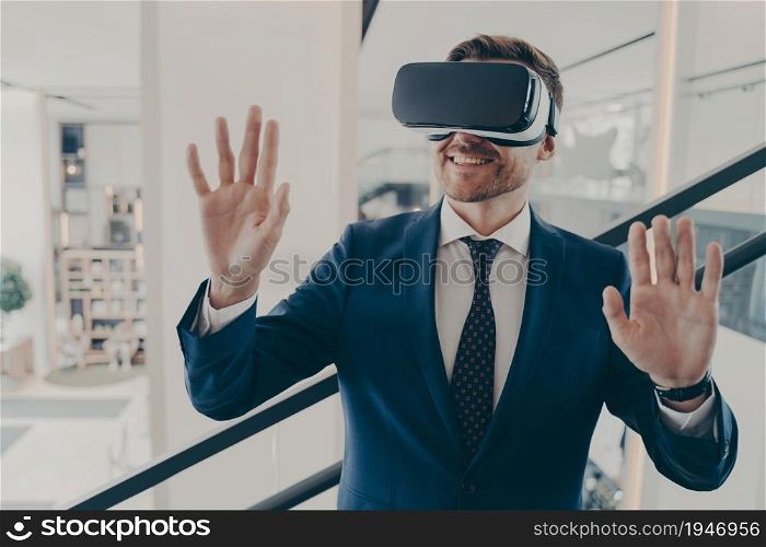 Young excited man office worker using virtual reality simulator at work, moving hands in air, being impressed of new innovative method in business, working with VR headset in digital actuality. Young excited man office worker using virtual reality simulator at work, moving hands in air
