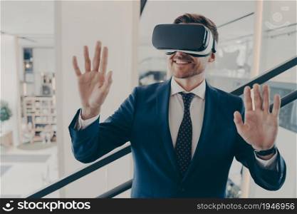 Young excited man office worker using virtual reality simulator at work, moving hands in air, being impressed of new innovative method in business, working with VR headset in digital actuality. Young excited man office worker using virtual reality simulator at work, moving hands in air
