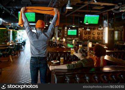 Young excited overjoyed friends watching football match in sports bar. Cheerful young people spending time together rear view. Young excited overjoyed friends watching football match in sports bar