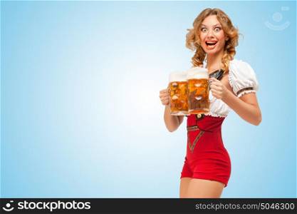 Young excited sexy Swiss woman wearing red jumper shorts with suspenders in a form of a traditional dirndl, serving two beer mugs on blue background.