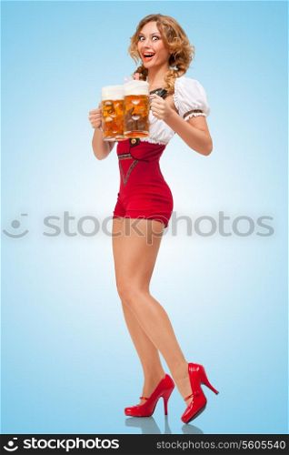 Young excited sexy Swiss woman wearing red jumper shorts with suspenders in a form of a traditional dirndl, serving two beer mugs on blue background.