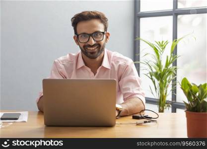 Young executive sitting in his cabin smiling while working on his laptop