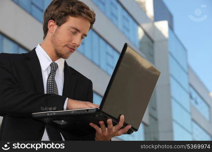 Young executive using a laptop outside an office building