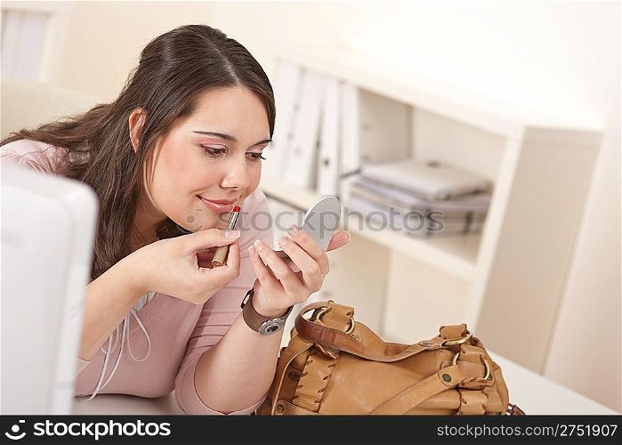 Young executive woman applying lipstick at modern office