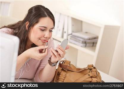 Young executive woman applying lipstick at modern office