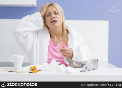 Young exhausted woman suffering from headache and cold in kitchen