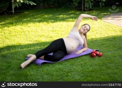 Young expectant mother stretching before yoga on grass at park