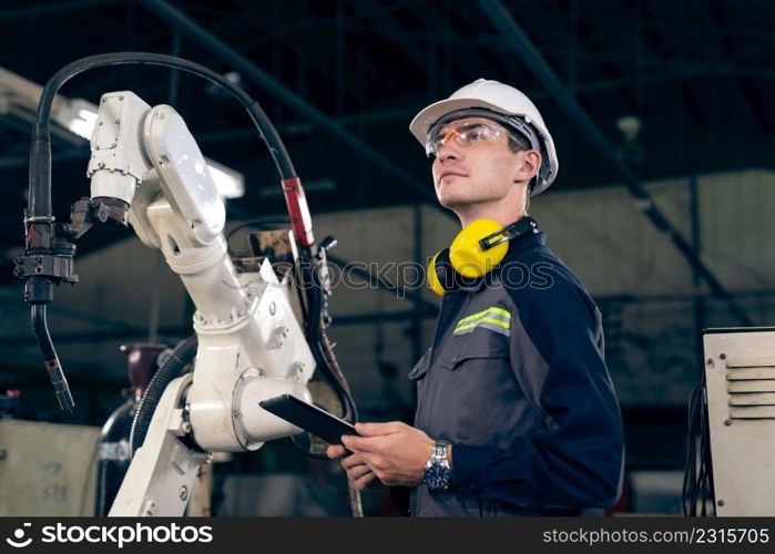 Young factory worker working with adept robotic arm in a workshop . Industry robot programming software for automated manufacturing technology .. Young factory worker working with adept robotic arm