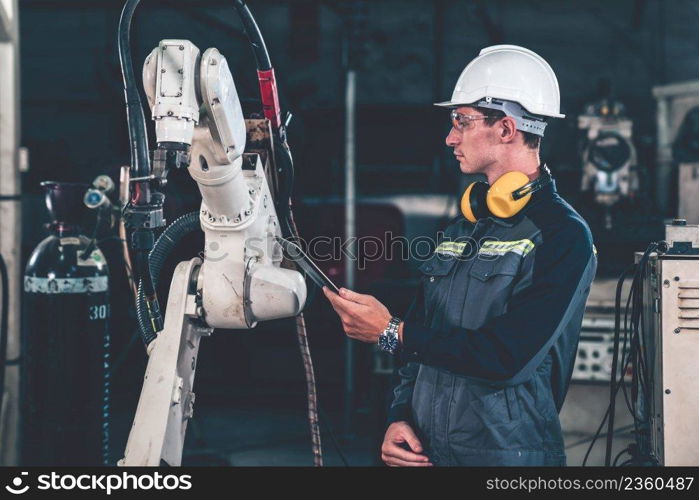 Young factory worker working with adept robotic arm in a workshop . Industry robot programming software for automated manufacturing technology .. Young factory worker working with adept robotic arm