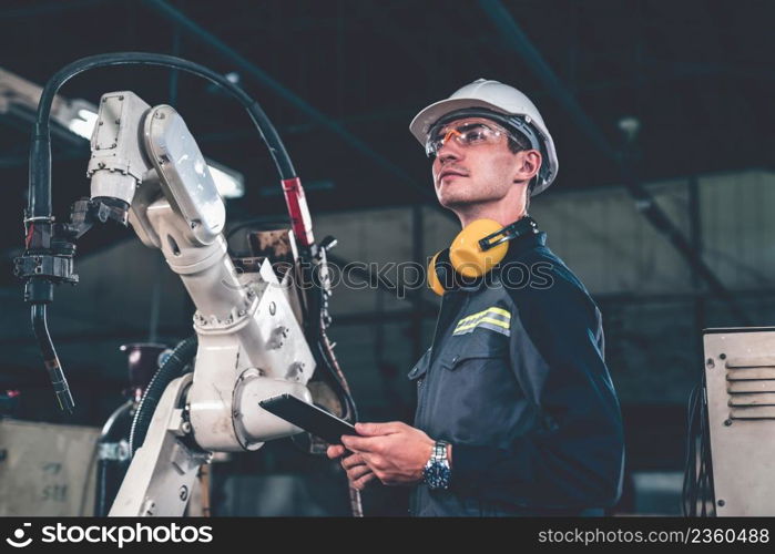 Young factory worker working with adept robotic arm in a workshop . Industry robot programming software for automated manufacturing technology .. Young factory worker working with adept robotic arm