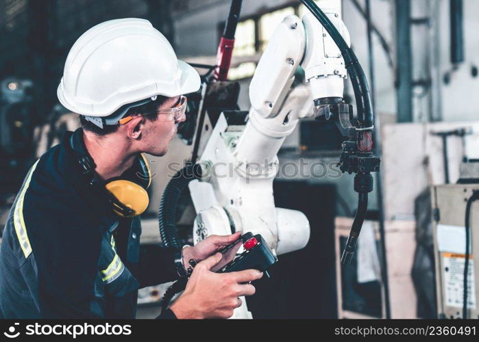 Young factory worker working with adept robotic arm in a workshop . Industry robot programming software for automated manufacturing technology .. Young factory worker working with adept robotic arm