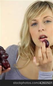 Young fair-haired woman eating grapes