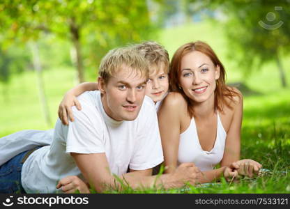 Young family consisting of three persons lies on a summer lawn