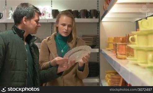 Young family couple choosing dishware in the store. Customers examining glass dish, ceramic plate and leaving