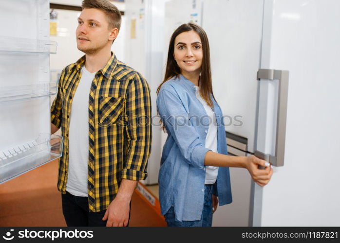 Young family couple choosing refrigerator in electronics store. Man and woman buying home electrical appliances in market. Young couple choosing refrigerator in store