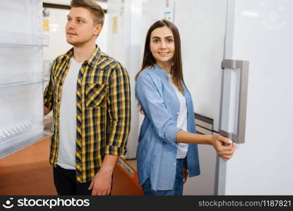 Young family couple choosing refrigerator in electronics store. Man and woman buying home electrical appliances in market. Young couple choosing refrigerator in store