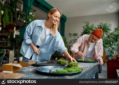 Young family couple of floral designer composing fresh cut green platter using moss and fern leaves. Craft art workshop design interior. Young family couple of floral designer composing fresh cut green platter